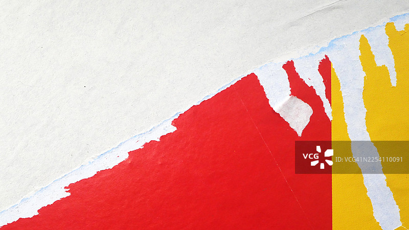 特写镜头,一张贴在墙上被撕毁的白色、红色和黄色海报。粗糙的纹理。自然光和色彩。法国巴黎。图片素材