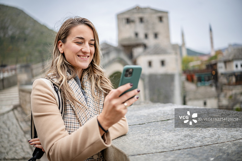 阴天时，一位年轻女子在访问波斯尼亚和黑塞哥维那的历史名城莫斯塔尔时查看手机图片素材