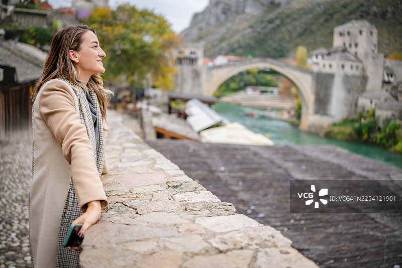 阴天里，一位年轻女子正在欣赏波斯尼亚和黑塞哥维那莫斯塔尔老桥的景色图片素材