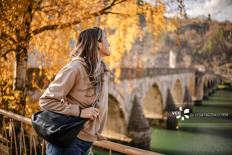 秋日晴朗，年轻女子欣赏波黑维谢格拉德大桥的景色图片素材