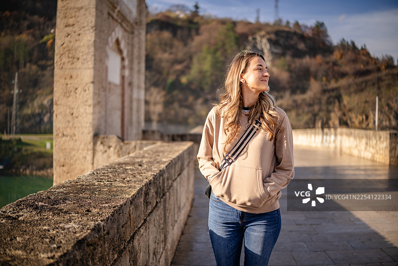 年轻女子在阳光明媚的日子里，漫步于波斯尼亚和黑塞哥维那维谢格拉德的历史悠久的桥上图片素材