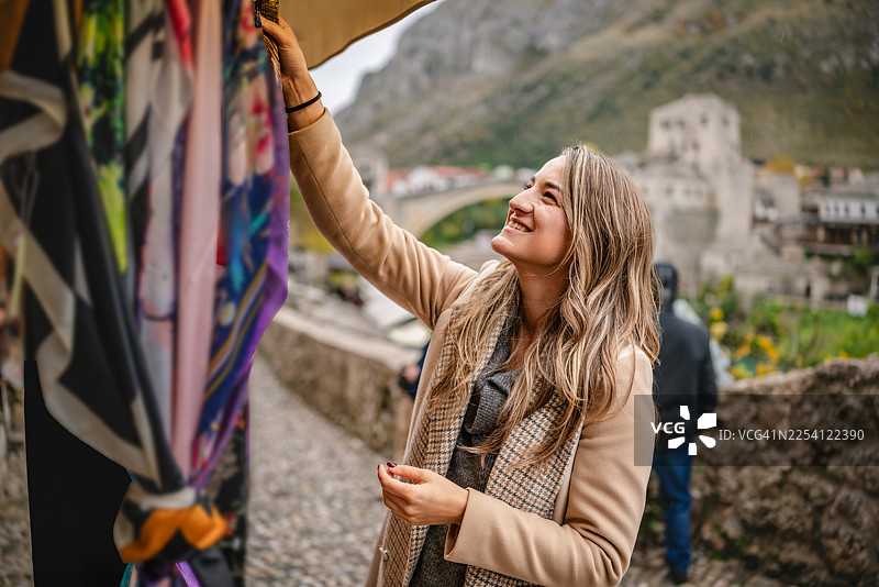 年轻女子在波斯尼亚和黑塞哥维那的莫斯塔尔，一边逛着充满活力的户外市场，一边欣赏当地的商品。图片素材