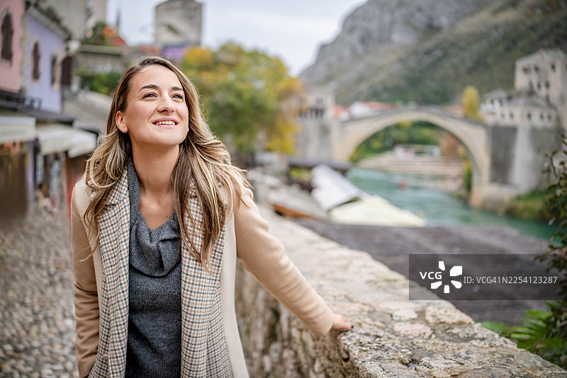 年轻女子在波斯尼亚和黑塞哥维那莫斯塔尔户外游览时，欣赏着河流和桥梁的景色图片素材