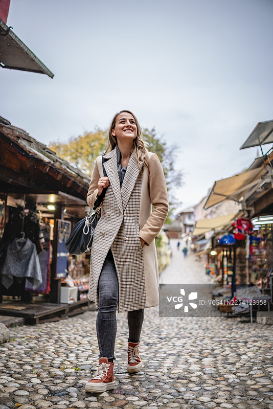 年轻女子在波斯尼亚和黑塞哥维那的莫斯塔尔鹅卵石街道上漫步，享受在市场中的旅行体验图片素材
