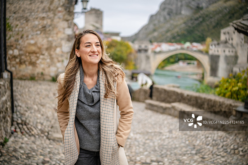 一位年轻女子在薄雾笼罩的日子里，于波斯尼亚和黑塞哥维那莫斯塔尔老桥附近探索街道图片素材