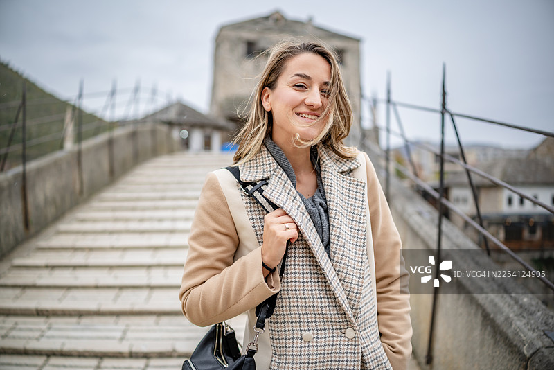 一位年轻女子在波斯尼亚和黑塞哥维那的莫斯塔尔桥上，在阴天中微笑着行走图片素材