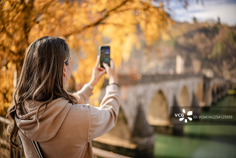 一位年轻女子在秋天于波斯尼亚和黑塞哥维那的维舍格勒德拍摄桥梁的照片图片素材