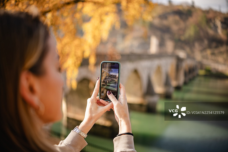 秋季，一位年轻女子在波斯尼亚和黑塞哥维那河边拍摄维谢格拉德的风景图片素材