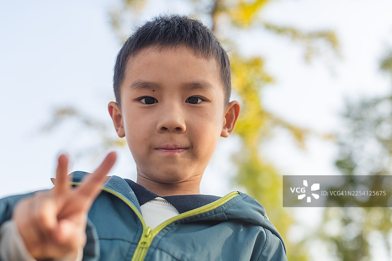 男孩在公园里比出和平手势的肖像图片素材