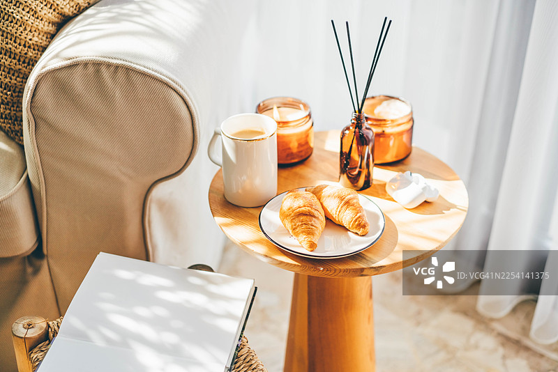 阳光沐浴下的木质边桌，摆放着咖啡和羊角面包，营造出舒适的晨间氛围。图片素材