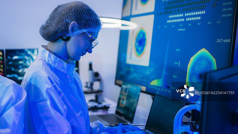 一位身穿无菌防护服的专业技术人员在无尘室的半导体制造工厂内，戴着手套检查色彩鲜艳的反射性半导体晶圆，代表着先进的微芯片技术和质量控制。图片素材