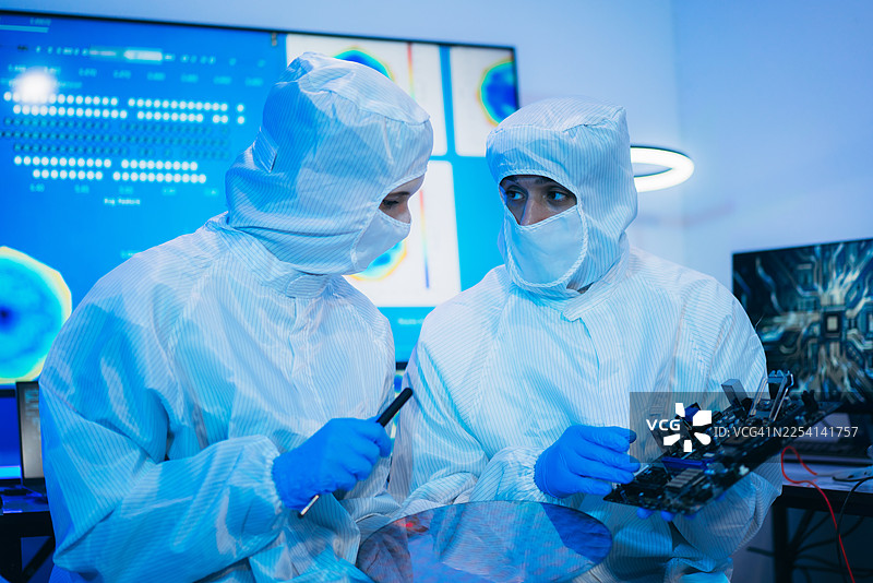 专业技术人员身着无菌防护服，戴着手套，在半导体制造厂的洁净室内检查彩色反光半导体晶圆，代表了先进的微芯片技术和质量控制。图片素材