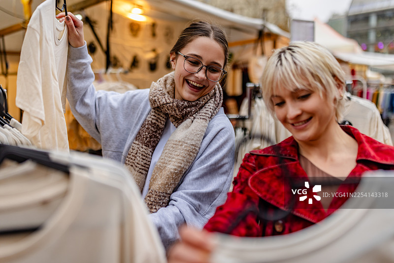 两位成年人在柏林的市场里购物，他们在一处繁忙的零售环境中看着陈列的服装，脸上带着笑容。图片素材