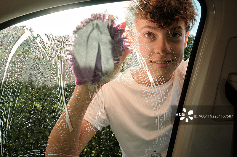 小男孩用沾满肥皂的手套清洗汽车车窗图片素材