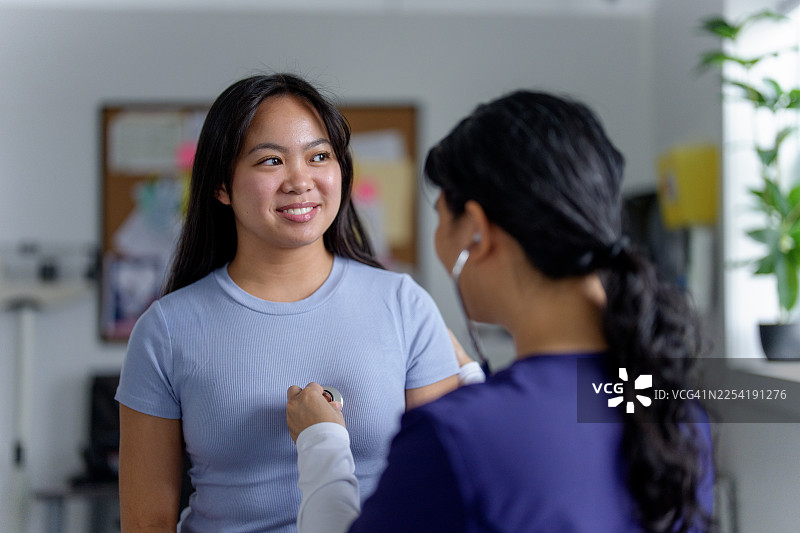 年轻亚洲女性在诊所接受体检，护士正在听她的心跳图片素材