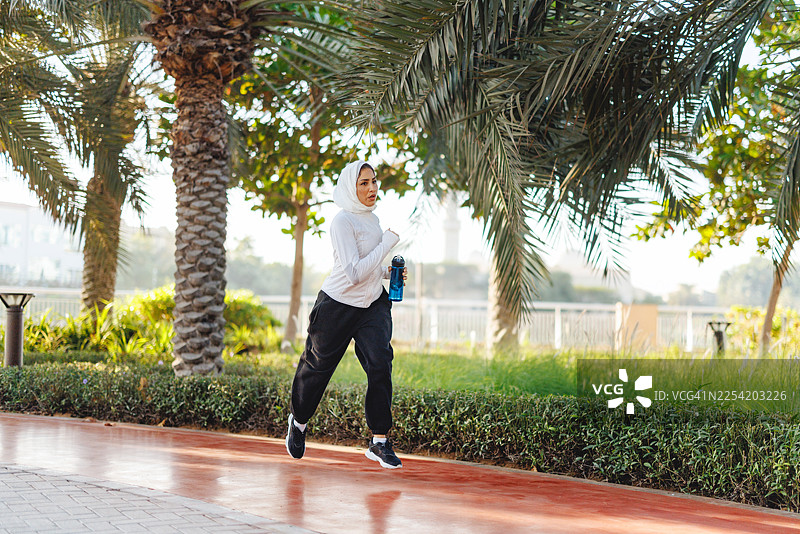 迪拜晨光中，年轻的穆斯林女性在林荫小道上慢跑图片素材