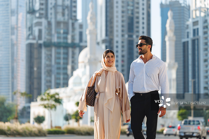 时尚的中东夫妇在自然日光下漫步于现代迪拜城市景观中图片素材