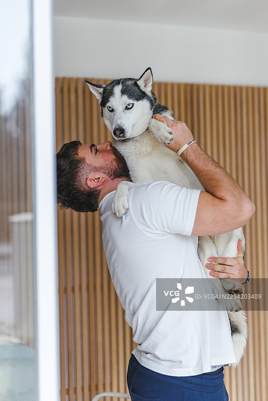 年轻的商务人士在带有木板背景的明亮现代办公室里抱着一只西伯利亚雪橇犬图片素材