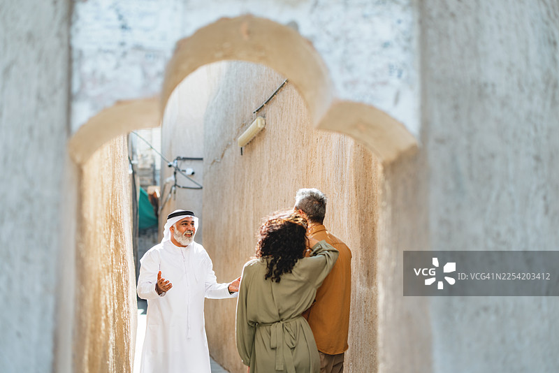 年长的阿拉伯导游在历史悠久的Al Fahidi街区与一对中年夫妇互动图片素材