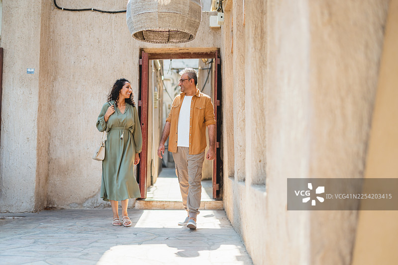 好奇的中东夫妇漫步在迪拜老城的质朴街道上，背景是米色墙壁图片素材