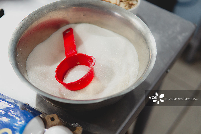 白色砂糖放在金属碗中，旁边配有红色量杯图片素材