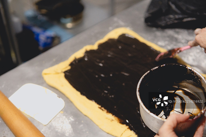 在糕点面团上涂抹巧克力馅料制作甜卷图片素材