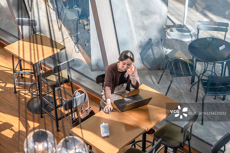一位快乐的女商人在咖啡馆用笔记本电脑工作。一位专业的自由职业者在舒适的咖啡馆环境中戴着眼镜使用笔记本电脑，享受着她的工作。图片素材