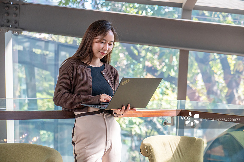 一位快乐的女商人在咖啡馆里用笔记本电脑工作。一位专业的自由职业者戴着眼镜，在舒适的咖啡馆环境中享受工作。图片素材