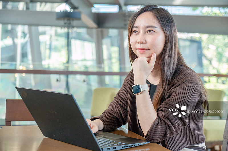 快乐的女商人正在咖啡馆用笔记本电脑工作。一位专业的自由职业者戴着眼镜，在舒适的咖啡馆环境中愉快地使用笔记本电脑工作。图片素材