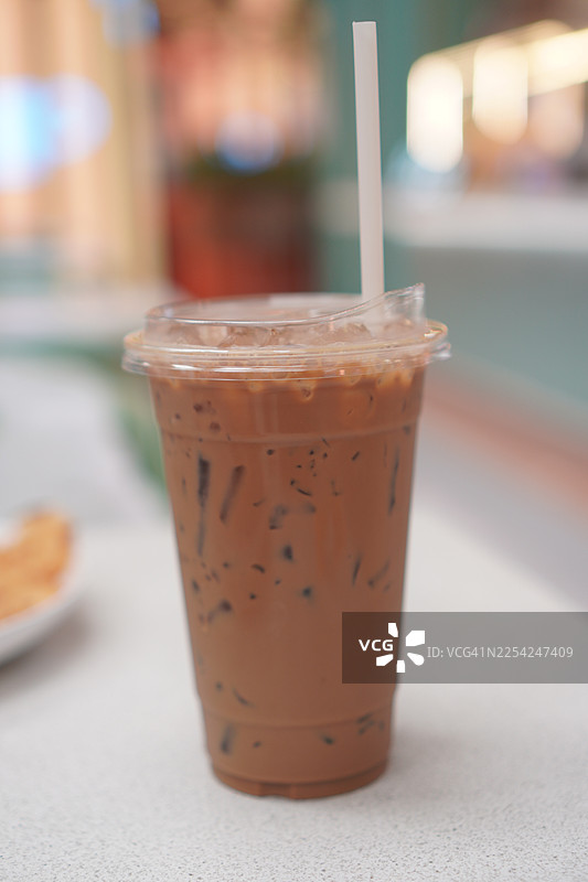 特写冷萃咖啡中的冰块，卡布奇诺装在塑料杯中，放在白色的桌子上，背景虚化，饮品图片素材
