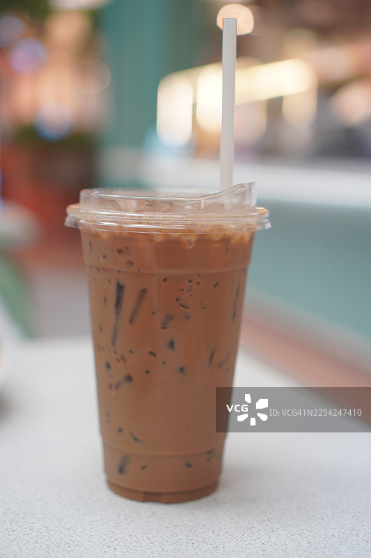 冷萃咖啡加冰块的特写，塑料杯装的卡布奇诺放在白色桌子上，背景模糊，饮品图片素材