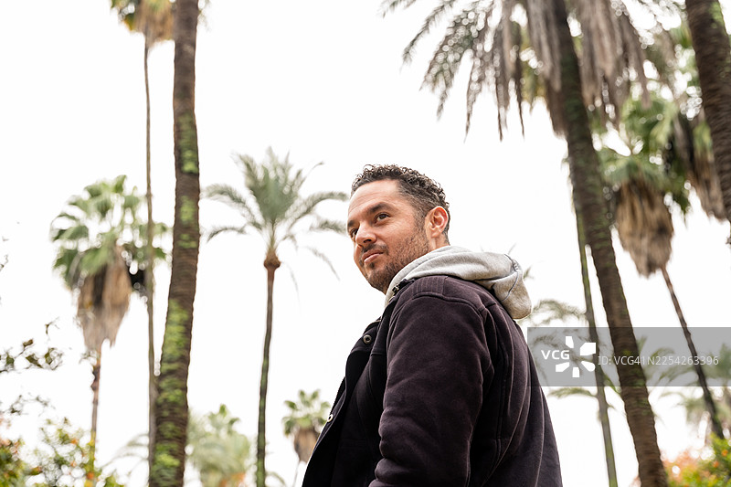 男人背对着镜头，周围环绕着热带棕榈树图片素材