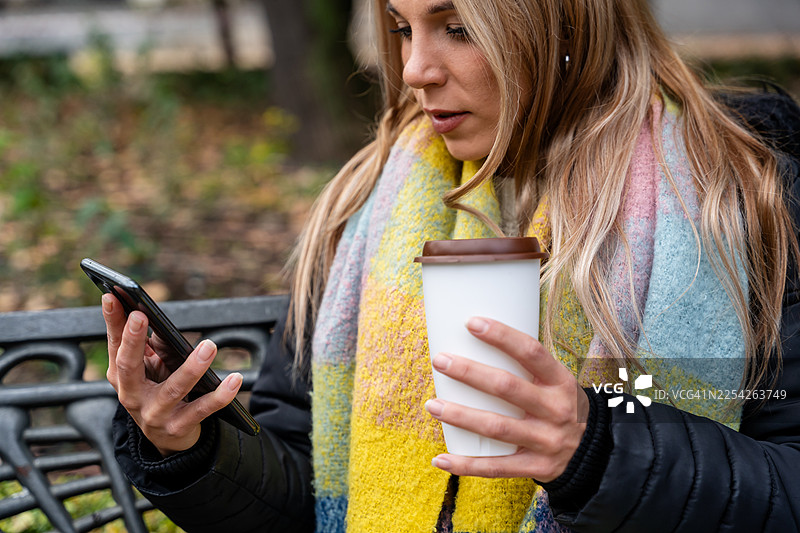 女人在公园里享受咖啡并查看智能手机图片素材