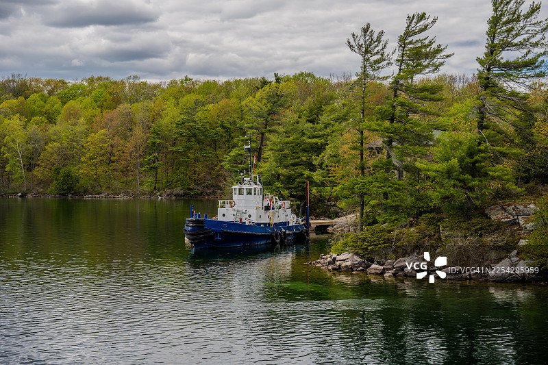 停靠在宁静湖泊、森林岩石海岸边的小型拖船图片素材