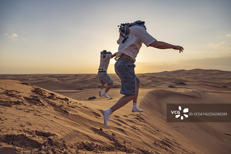 青少年游客在迪拜沙漠冲沙日落时分，奔跑跳跃在沙丘上图片素材
