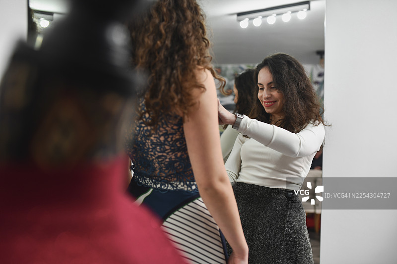 时尚工作室试衣环节：设计师在客户试穿优雅连衣裙时为其量体。图片素材