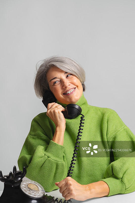 一位成熟的成年女性微笑着使用老式旋转电话图片素材
