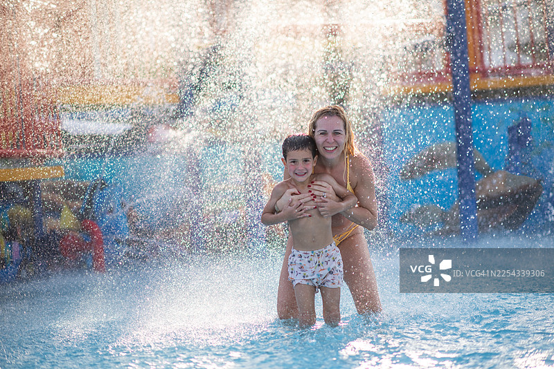 一位活跃的母亲和一个微笑的男孩在水上乐园玩耍。图片素材