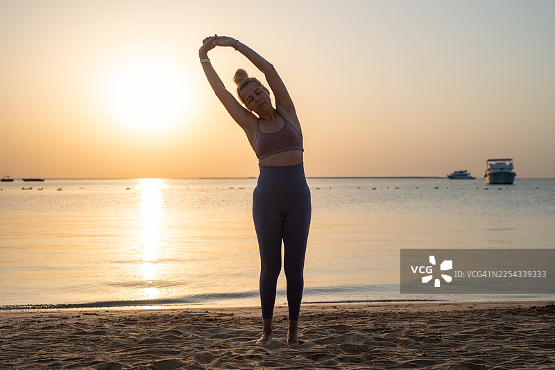 一位美丽的女子在美丽的日出时分，于沙滩上进行侧弯伸展，寻找平衡与宁静。图片素材