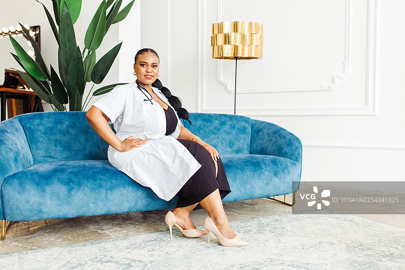 一位自信的女医生坐在明亮现代健康工作室的蓝色沙发上图片素材
