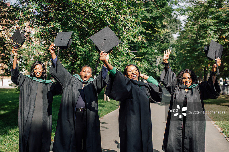 四名毕业生在户外穿着毕业礼服庆祝成就，在欢乐的仪式中抛帽图片素材