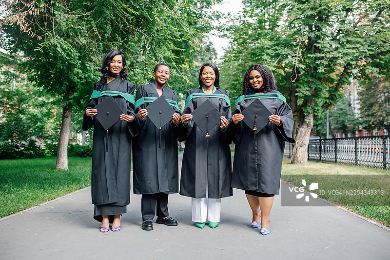 四位穿着毕业礼服和帽子的毕业生在户外合影，庆祝人生中的重要时刻图片素材