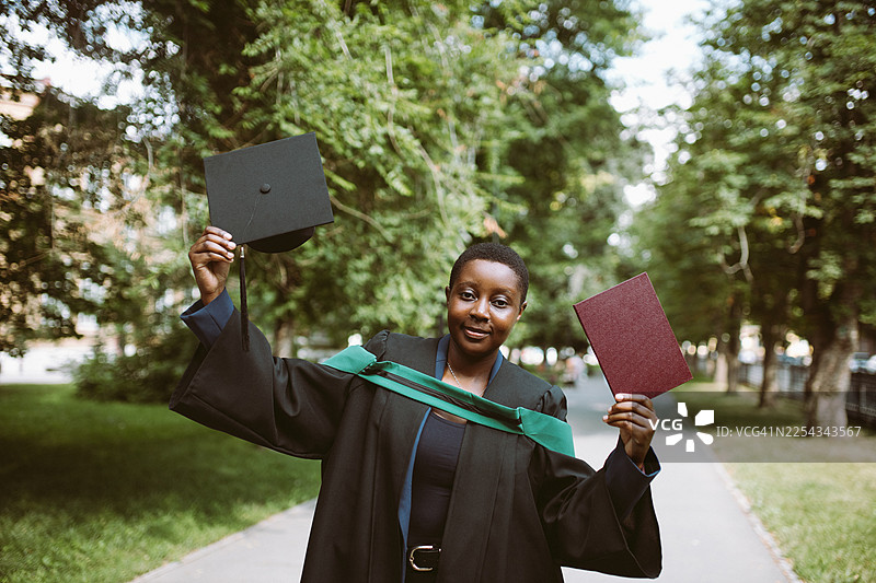 毕业典礼上，毕业生自豪地在户外校园里手持学士帽和毕业文凭图片素材