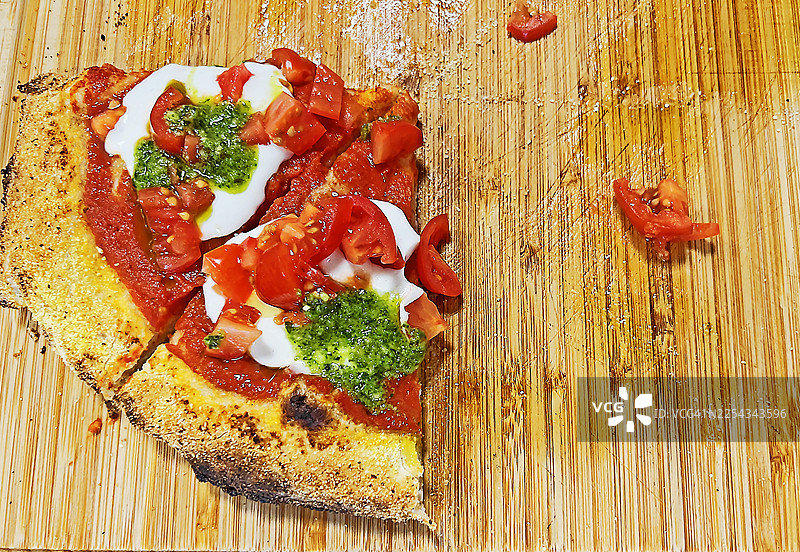 木板上只剩下两片单独的披萨。番茄、马苏里拉奶酪、香蒜酱和橄榄油。俯视角度。图片素材