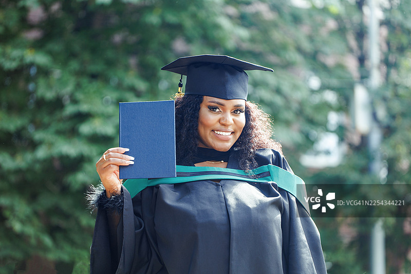 身着毕业礼服的毕业生在户外手持毕业文凭，庆祝成就与成功图片素材