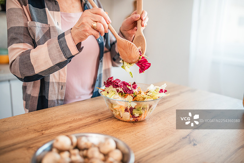 特写镜头：一位无法辨认的老妇人正用木勺在碗里搅拌沙拉。图片素材