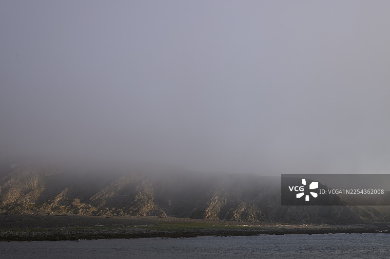 雾气笼罩的海岸景观,岩石营造出神秘而阴郁的氛围,位于挪威芬马克郡的巴特斯峡湾图片素材