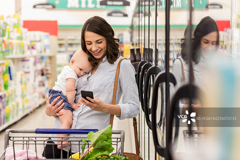 一位母亲在超市过道推着婴儿车，同时使用手机图片素材