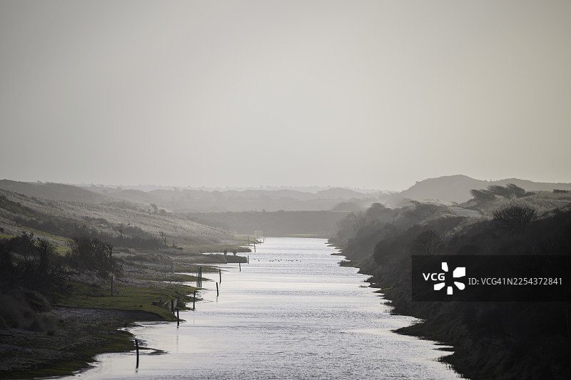 黄昏时分，雾蒙蒙的单色沙丘景观中，阿姆斯特丹水利运河（Amsterdamse Waterleidingduinen）平静的水面倒影，位于荷兰北荷兰省赞德福特。图片素材