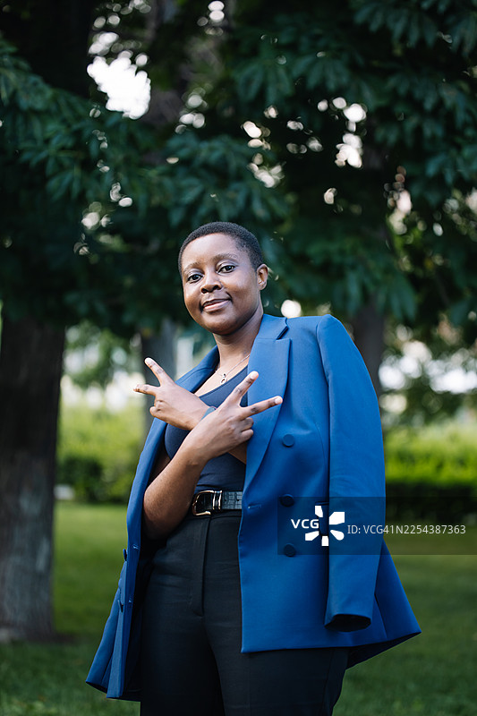 自信的女士身穿蓝色西装外套，在户外摆出胜利手势并微笑图片素材